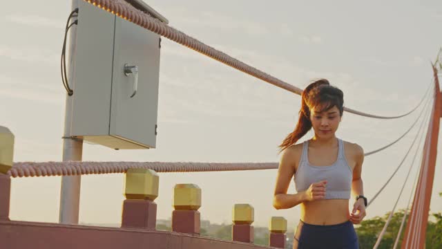 亚洲年轻美丽的女人在傍晚的夕阳在大桥在公共公园跑步健康。运动员健康和坚定的女孩锻炼通过慢跑锻炼户外运动为她的健康。
