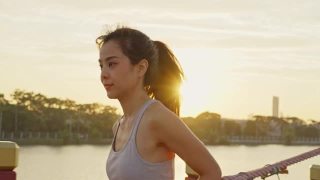亚洲年轻美丽的女人在傍晚的夕阳在大桥在公共公园跑步健康。运动员健康和坚定的女孩锻炼通过慢跑锻炼户外运动为她的健康。视频素材模板下载