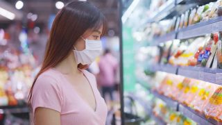 亚洲妇女戴着口罩，拿着购物篮在超市购物。在冠状病毒危机或新冠肺炎爆发期间，女孩在货架上挑选、寻找食物。视频素材模板下载