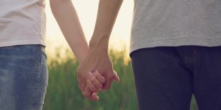 近距离拍摄的一对亚洲男人和女人站在一起，牵着对方的手，然后在美丽的夕阳下慢慢摇摆。蜜月约会的概念。