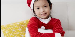 快乐的亚洲女孩穿着圣诞老人服装，坐在家里的沙发上，生活理念。