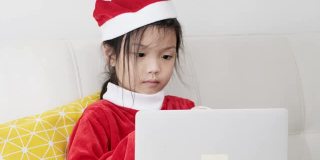 快乐的亚洲女孩穿着圣诞老人服装，坐在家里的沙发上，生活理念。