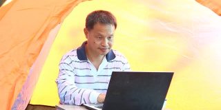 一个泰国人在帐篷里用笔记本电脑工作