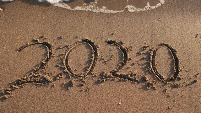 我们将度过非常糟糕的一年。写在沙滩上的2020消失在海浪中。再见2020欢迎2021