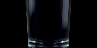 将一片维生素C药片倒入一个透明的玻璃玻璃杯中，加入水。这起泡的黄色药片溶化了。黑色背景上的玻璃。缓慢的运动。近距离
