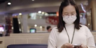 亚洲商界女性戴口罩预防冠状病毒感染。使用智能手机了解COVID-19疫情。在社区或餐厅保持社交距离。医疗保健新常态