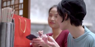 亚洲幸福女人吃饺子和玩手机在户外桌子café。概念时尚女孩的生活方式。