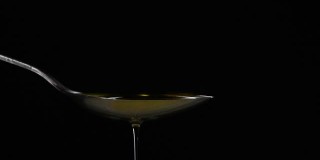 特写将橄榄油液体倒入勺子在黑色背景的慢动作