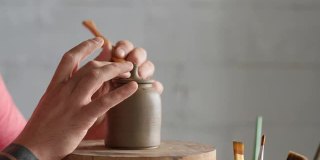 陶工把一个把手装在陶工轮上的陶壶盖上。手工制作的陶器。陶工制作粘土制品