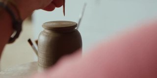 一个专业的陶工在一个陶工轮上的泥茶壶的盖子上做一个洞。手工制作的。艺术工艺。工艺工作的概念