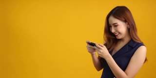 亚洲女性玩家在智能手机上玩在线游戏，黄色背景，娱乐与令人敬畏的应用概念