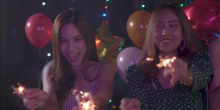 这是两名亚洲年轻女性在晚会上微笑和使用烟花的4k视频。妇女们在圣诞节和新年互相庆祝。