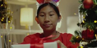 快乐亚洲女孩穿着红毛衣摇礼盒后收到来自家人用圣诞装饰在家里的生活理念。