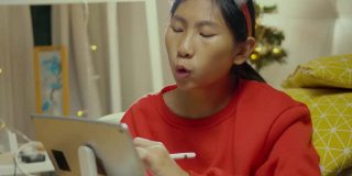快乐的亚洲女孩穿着红色的毛衣，唱歌和绘画的数字平板电脑在家里的圣诞装饰，生活理念。