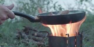 森林里野餐时，一名男子在篝火上用煎锅煎肉。