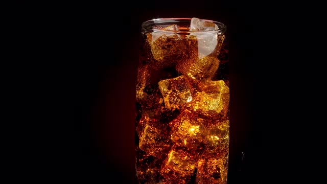 一杯可乐泡泡加冰块。可乐与冰和泡沫在玻璃上的黑色背景。