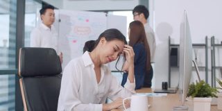在现代化的小办公室里，女商人们在会议室的电脑桌面上忙着项目研究。亚洲人职业倦怠综合症的概念。