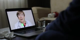女医生在家客厅通过笔记本电脑听病人视频聊天。男子与医生视频聊天