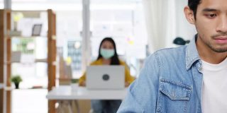 新常态下的亚洲商人社交距离为病毒预防在家庭办公室工作时使用笔记本电脑向同事介绍视频通话计划。