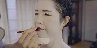 一名日本女性为艺妓化妆，涂上红唇