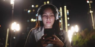 亚洲女性在晚上使用带耳机的智能手机