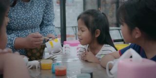 亚洲女孩和朋友们兴奋的时候，老师正在教用油彩在陶瓷玻璃上作画。孩子们在学校的艺术和手工艺创意活动班。