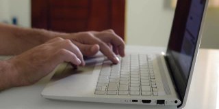 一个男人的手在一个笔记本电脑键盘上打字的特写，在一个家庭办公室的桌子上。
