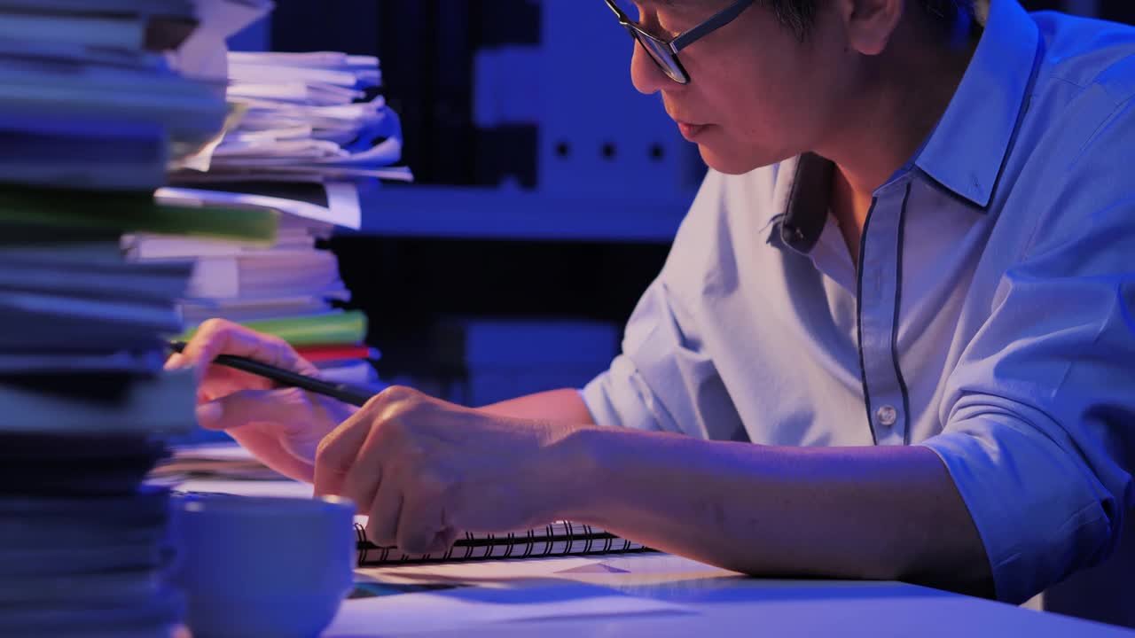 57岁的亚洲老年男性工作过度，感到疲劳不适，在办公桌上工作到深夜。在家工作的概念。