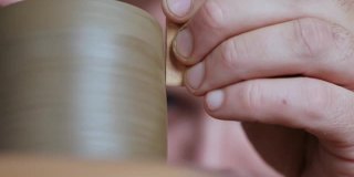 特写镜头。陶工在陶工轮上加工一个陶土茶壶的边缘。陶瓷艺术的概念。手工制作的陶器。陶工制作粘土制品