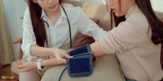 一位亚洲女医生正在给这位年轻的女病人在家测量血压。