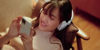 孤独的女孩戴着耳机，晚上在沙发上用智能手机选音乐。