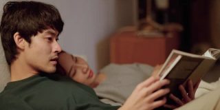 ็快乐的男朋友在睡觉前和疲惫的女人在舒适的床上读教科书。