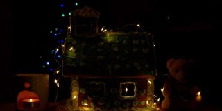用软熊装饰自制的甜饼屋，在香薰灯中点缀发光的蜡烛，散光的节日花环装饰模糊了圣诞树的散光灯的黑暗背景。新年前夜4K视频