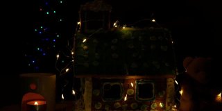 用软熊装饰自制的甜饼屋，在香薰灯中点缀发光的蜡烛，散光的节日花环装饰模糊了圣诞树的散光灯的黑暗背景。新年前夜4K视频