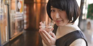 年轻女子在站着的“Tachinomi”酒吧喝日本“Saki”米酒