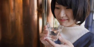年轻女子在站着的“Tachinomi”酒吧喝日本“Saki”米酒