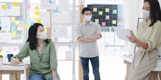 亚洲商务人士在新常态的办公室里开会，头脑风暴，进行商业演示，想法，项目同事，并戴上防护口罩。