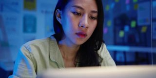 亚洲自由职业女性使用笔记本电脑在新的正常办公室努力工作。晚上在家超负荷工作。