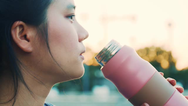 亚洲年轻女性在锻炼期间喝水，慢跑，在公园里跑步，近距离女性在锻炼后喝水。