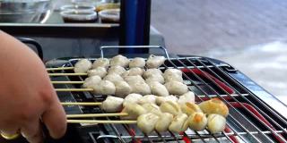 泰国街头小吃市场，摊贩的手正在用木炭炉烤肉丸和猪肉球。传统的泰国菜式。