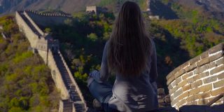一个年轻女子坐在中国长城上沉思的慢动作镜头。塔拉维尔到中国的概念
