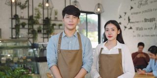 亚洲夫妇咖啡师或老板在围裙看着相机准备给咖啡服务在现代咖啡店