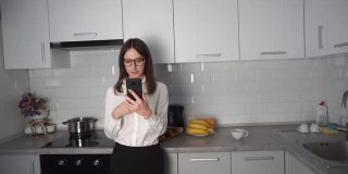 戴眼镜的女孩在厨房里用手机工作