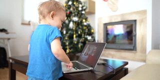蹒跚学步的孩子在与祖父母的视频通话中，在笔记本电脑旁跳舞。爷爷奶奶通过视频链接祝福小孙子圣诞快乐，新年快乐。新常态，居家理念