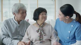 幸福的亚洲老年夫妇与在家庭护理坐在沙发微笑沙发看着相机与享受退休或隔离时间合影。亚洲老年人的生活方式。视频素材模板下载