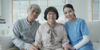 幸福的亚洲老年夫妇与在家庭护理坐在沙发微笑沙发看着相机与享受退休或隔离时间合影。亚洲老年人的生活方式。
