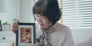 肖像快乐资深亚洲妇女放松坐微笑看着相框提醒过去的记忆在家里享受退休或隔离时间。亚洲成年老年人生活方式幸福。