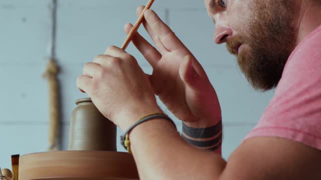 专业男性陶工在陶工轮上的陶壶盖上形成一个把手。艺术工艺。工艺工作的概念
