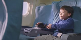 亚洲小男孩在飞机上触摸屏幕，然后看电影和卡通。孩子们感到高兴和兴奋的飞机旅行和享受机上娱乐。