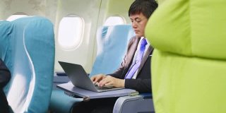 亚洲商人坐在商务舱在飞机上用笔记本电脑工作。男人很忙，眼睛感到很累。医疗保健关注和技术为商业人士的理念。